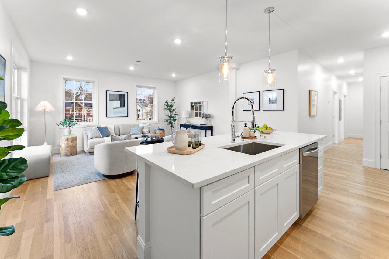 Open-plan kitchen and living area with a large white island and light wood floors.