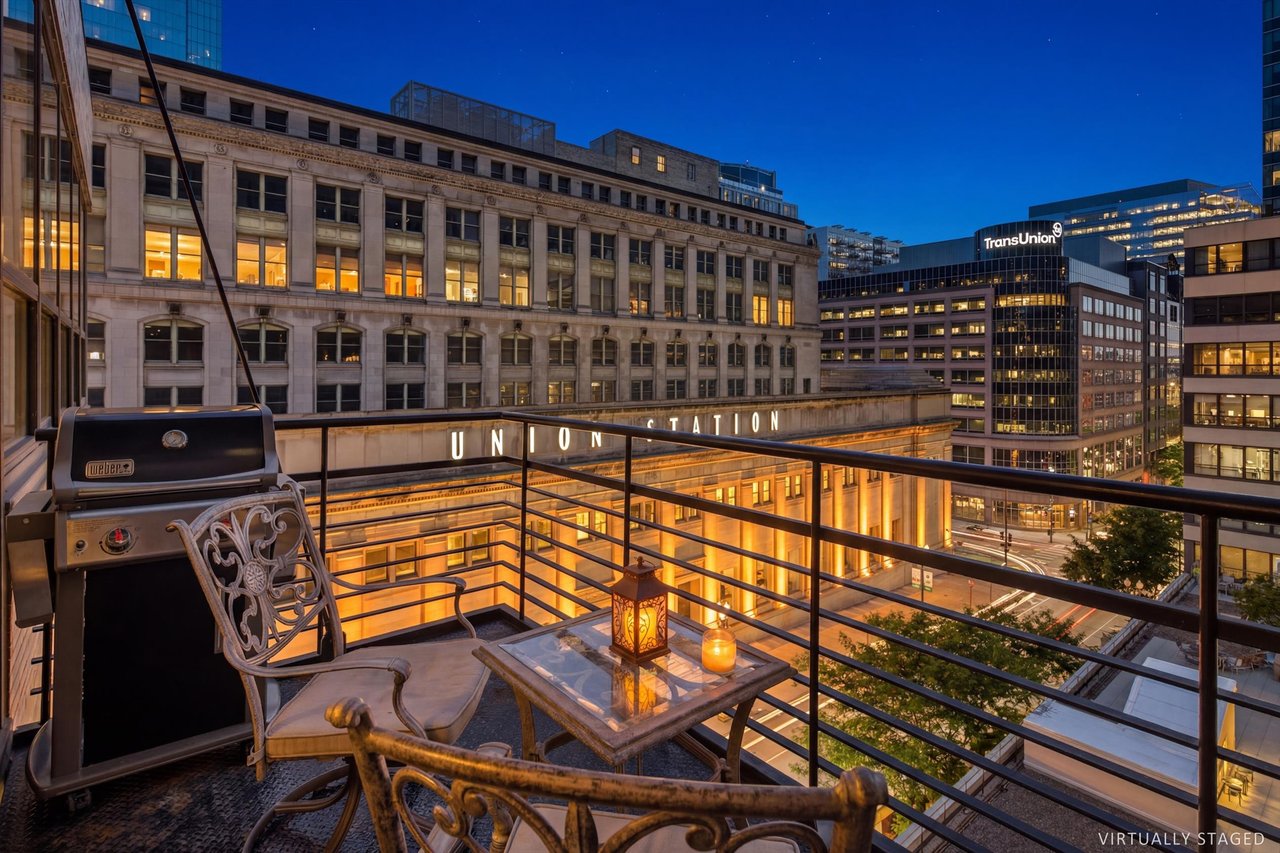 Balcony with patio seating and a grill overlooking illuminated downtown Chicago buildings at dusk.