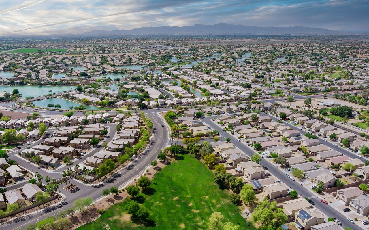 Aerial view of a suburban neighborhood with winding streets, water channels, and distant mountains.