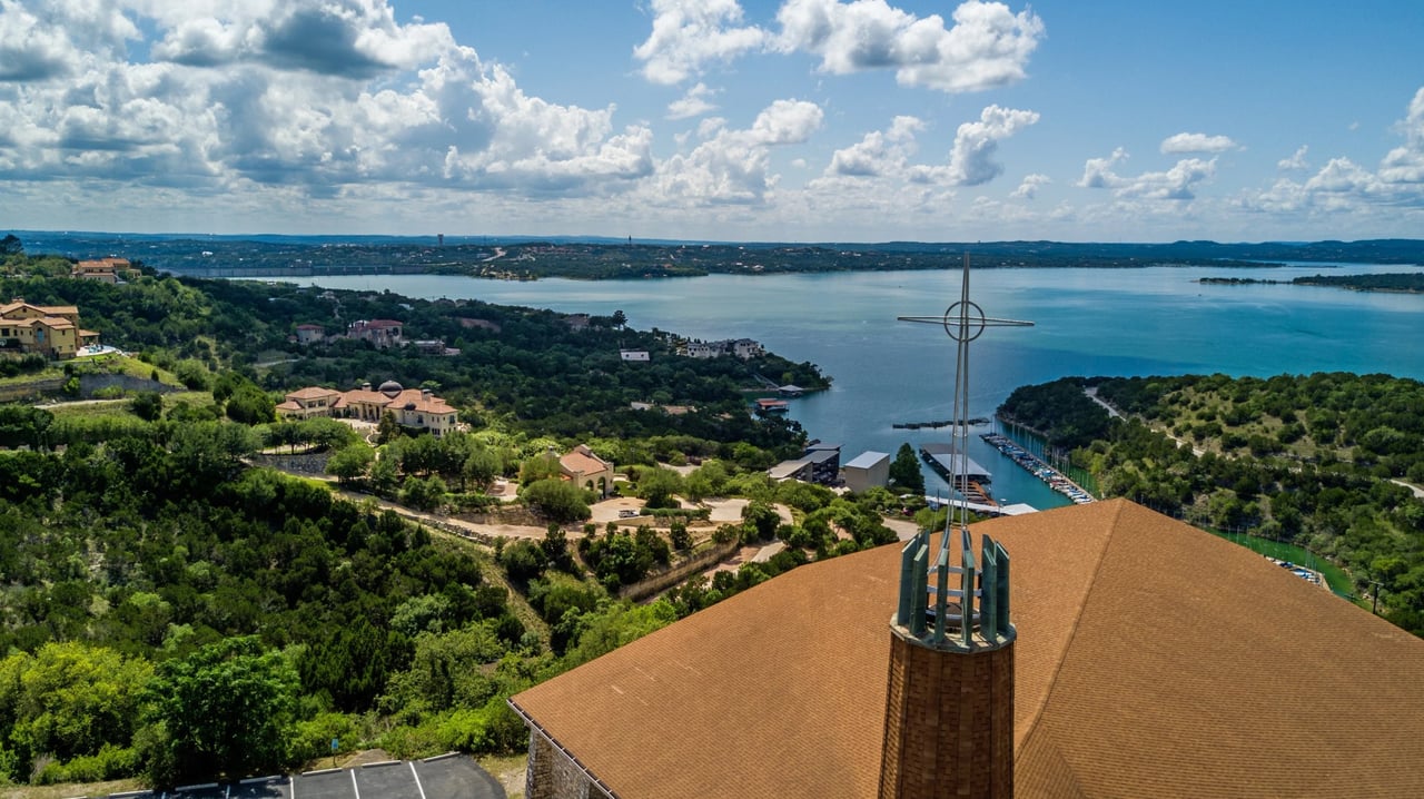 Aerial view of Lakeway homes and marina along the lake, with a church steeple in the foreground.