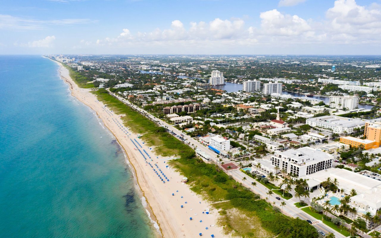 Aerial view of a sandy beach and coastal city beside turquoise ocean.