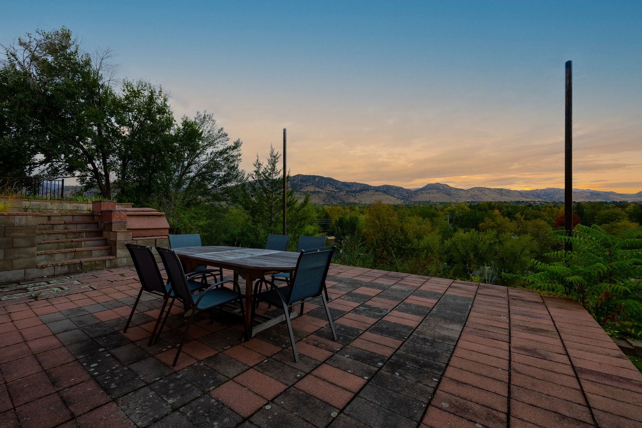 Brick patio with outdoor dining at 2003 Balsam Drive at dusk, overlooking trees and the foothills