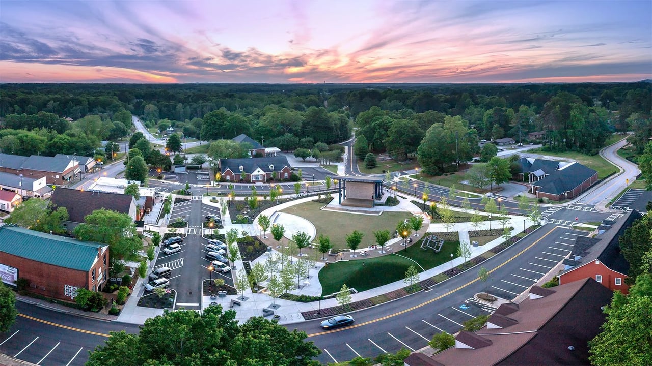 Aerial view of a landscaped town center with a pavilion and surrounding shops at dusk.