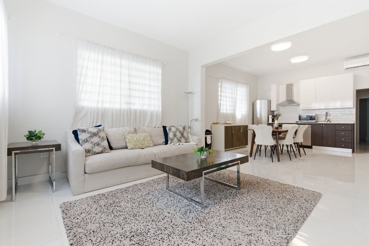 Open-plan living room with a white sofa and dark coffee table beside a dining area and kitchen.