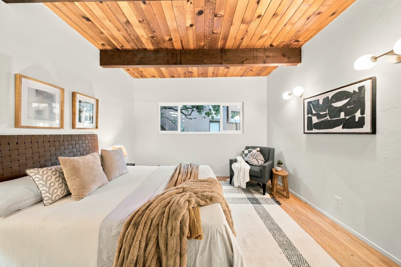 Bedroom with a wood-plank ceiling, upholstered bed, and gray armchair.