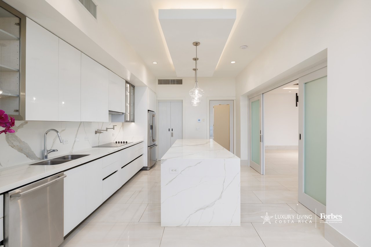 Modern white kitchen with a marble-veined waterfall island and stainless steel appliances.