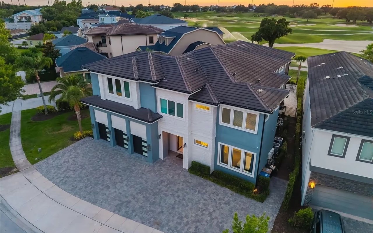 Aerial view of a blue-and-white two-story home beside a golf course at sunset.
