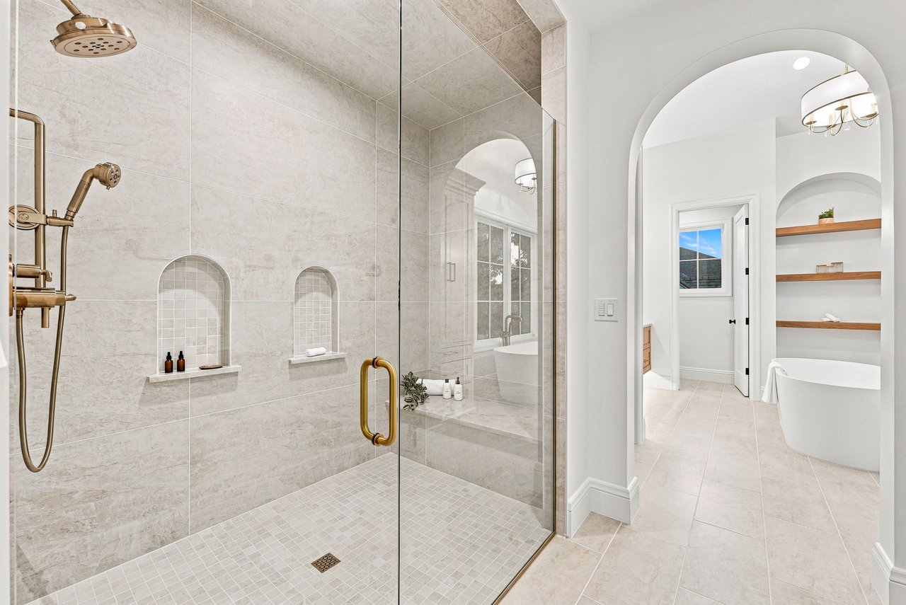 Bathroom with a glass-enclosed stone shower, brass fixtures, and an arched soaking tub alcove.