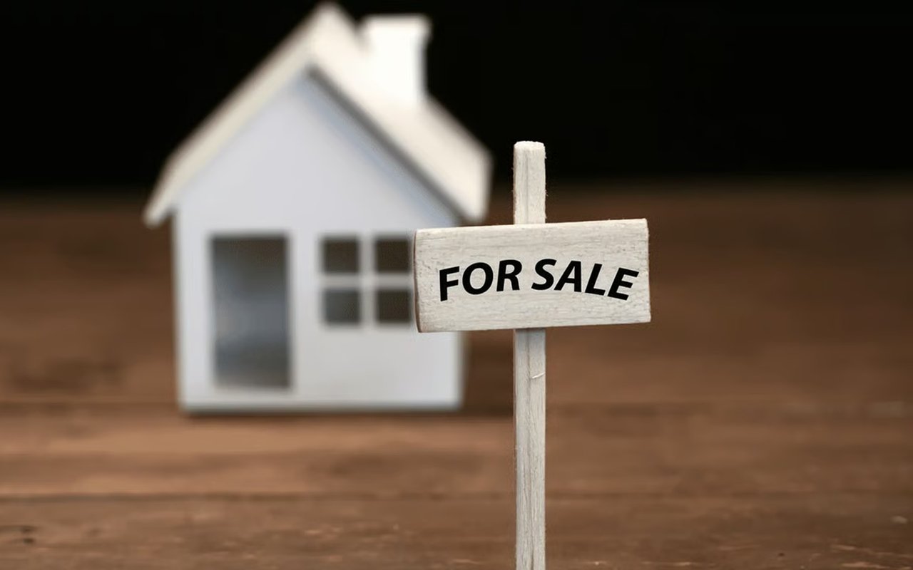 Miniature for-sale sign in front of a small white model house.