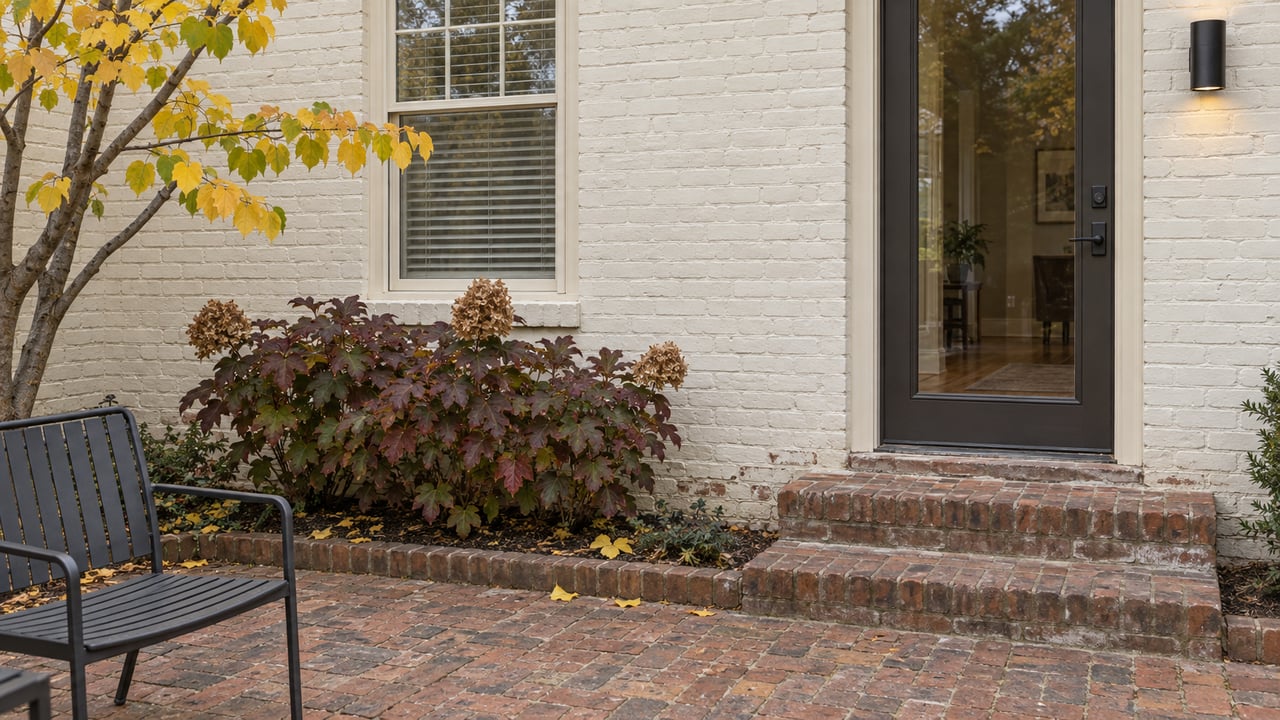 Painted brick home with a glazed back door, worn brick steps and terrace, and autumn oakleaf hydrangea.