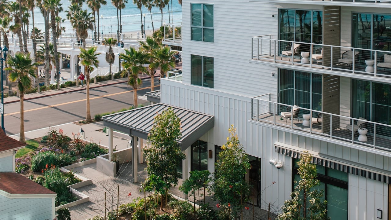 Coastal condominium exterior with balconies overlooking a palm-lined street and the ocean.