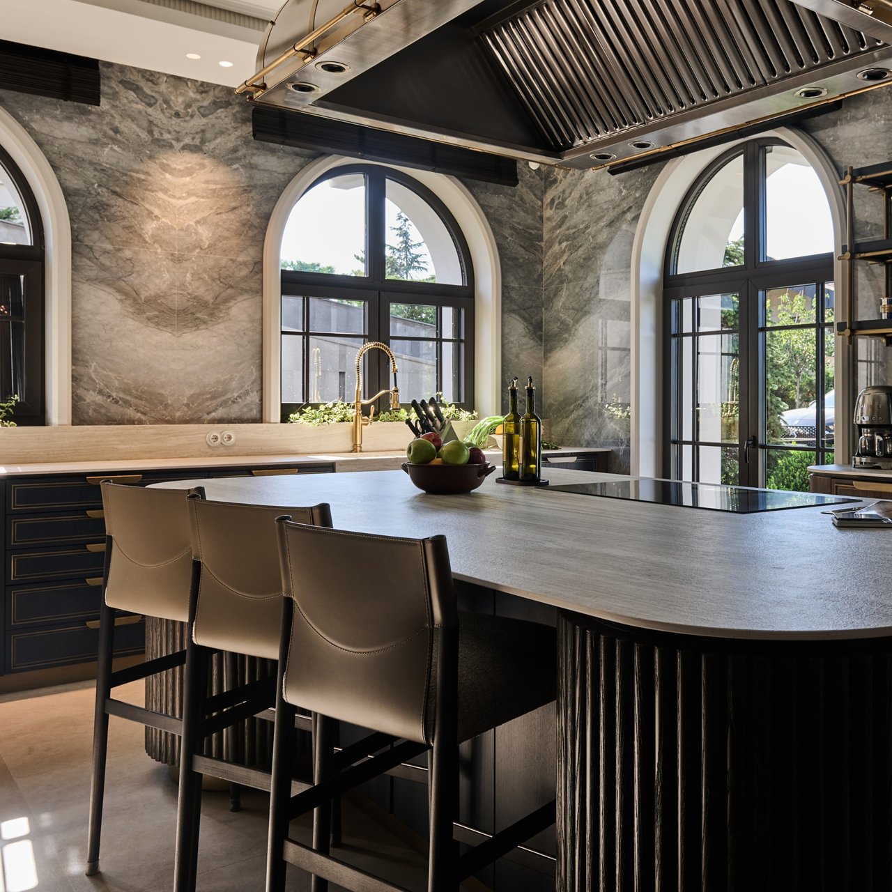 Luxury kitchen with a marble island, leather stools, and tall arched windows.