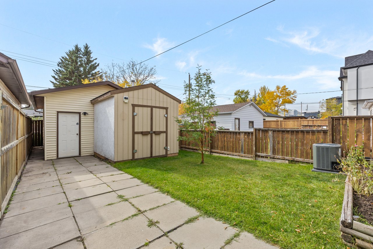 Fenced backyard with a large storage shed, paved patio path, and green lawn.