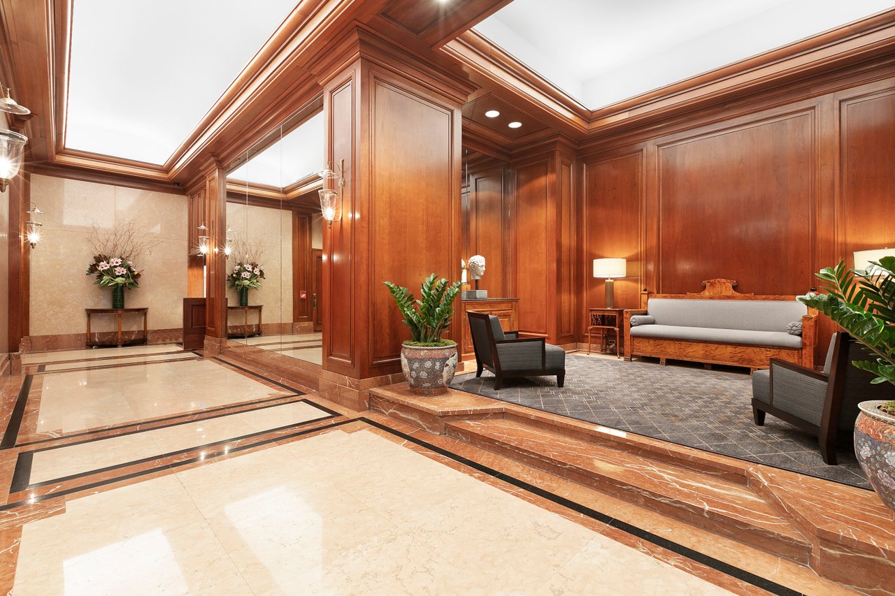 Building lobby with wood-paneled walls, marble flooring, mirrored wall, and a raised seating area.
