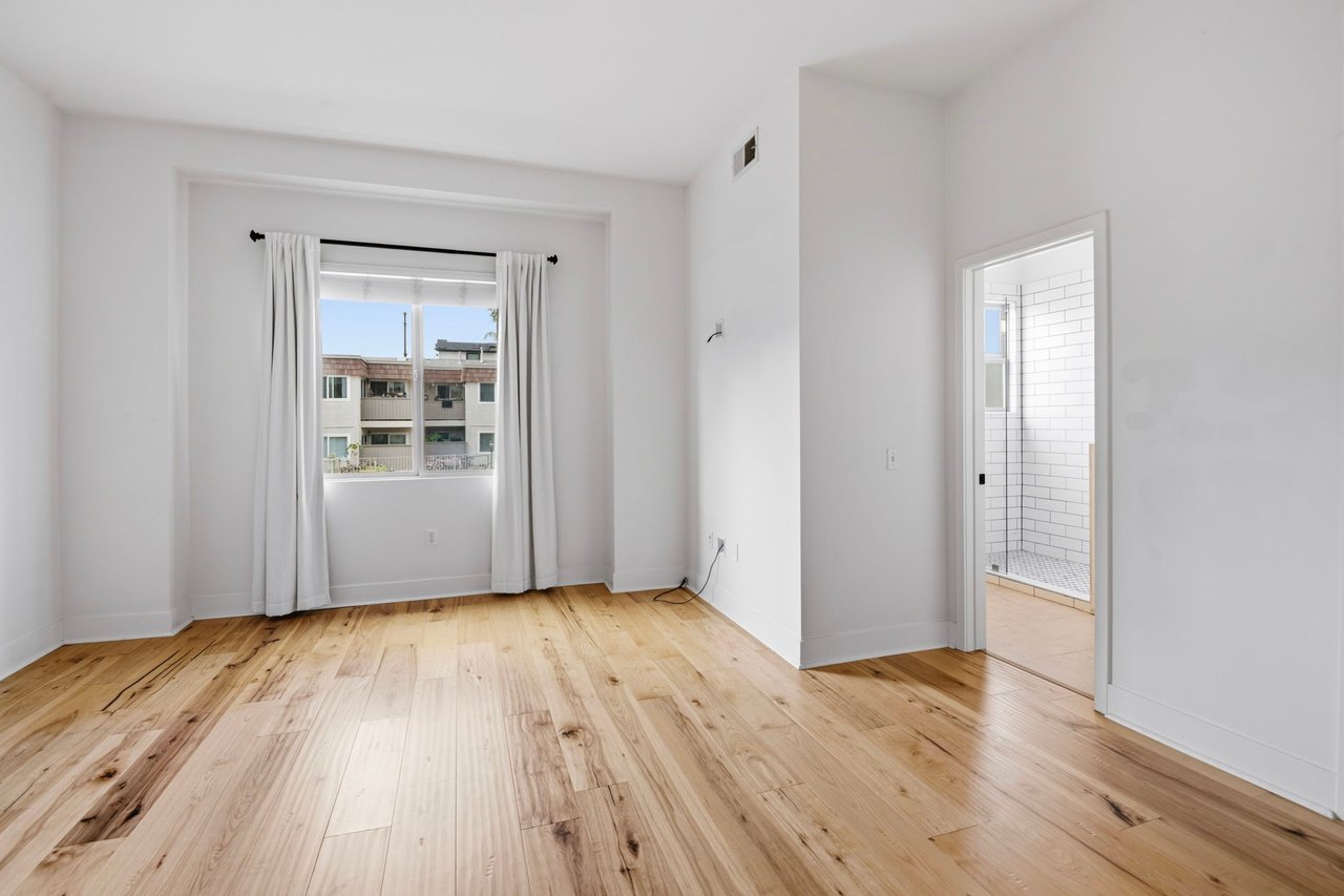 Primary bedroom with hardwood floors, French doors to private balcony, and en-suite bathroom access