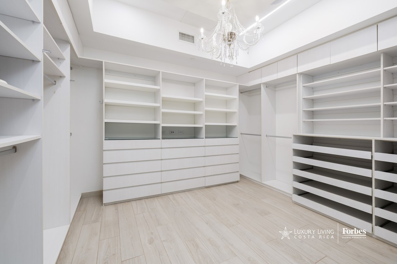 Walk-in closet with extensive white built-in storage, shoe racks, and a crystal chandelier.