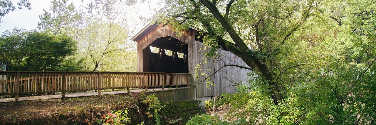 Historic wooden covered bridge at Ada Covered Bridge Park in Ada Michigan surrounded by trees and greenery.