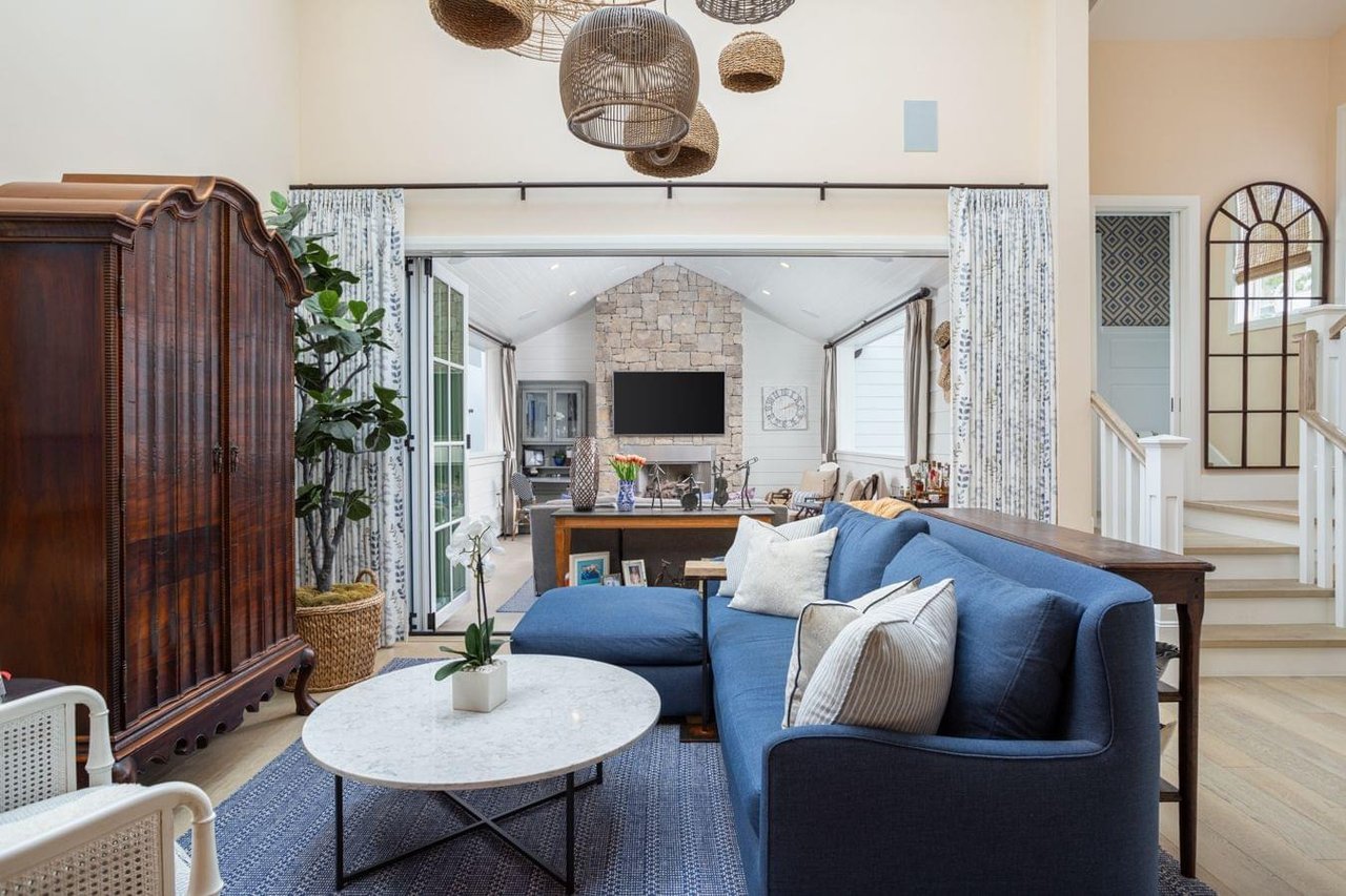  A large living room with a blue sectional sofa, a dark wood cabinet, and a view into a sunroom with a stone fireplace.