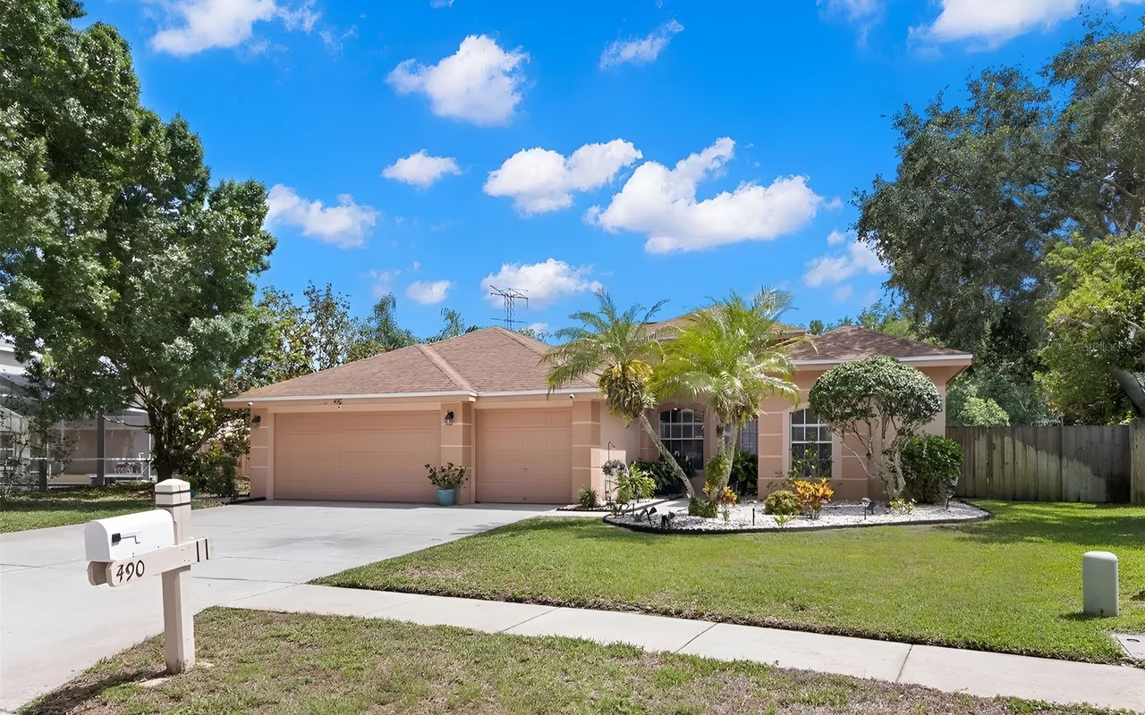 Single-story peach home with a three-car garage, palm trees, and a landscaped front yard.