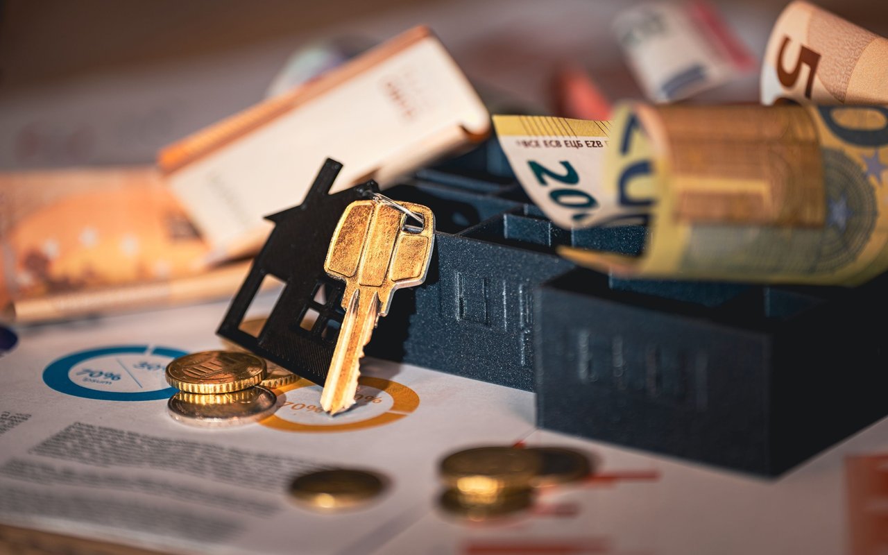 Model house and brass key among coins, paperwork, and rolled banknotes.