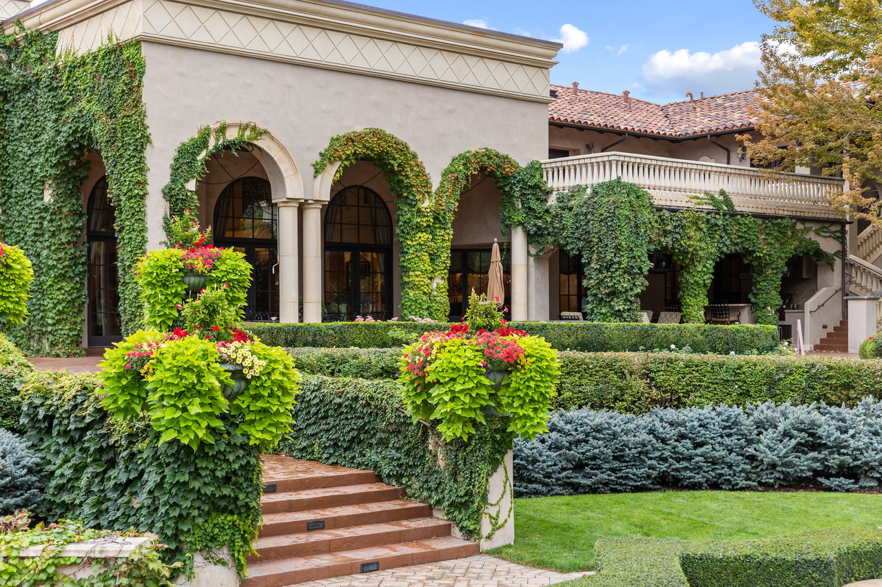 Landscaped garden steps lead to an ivy-covered estate with arched windows and flower planters.