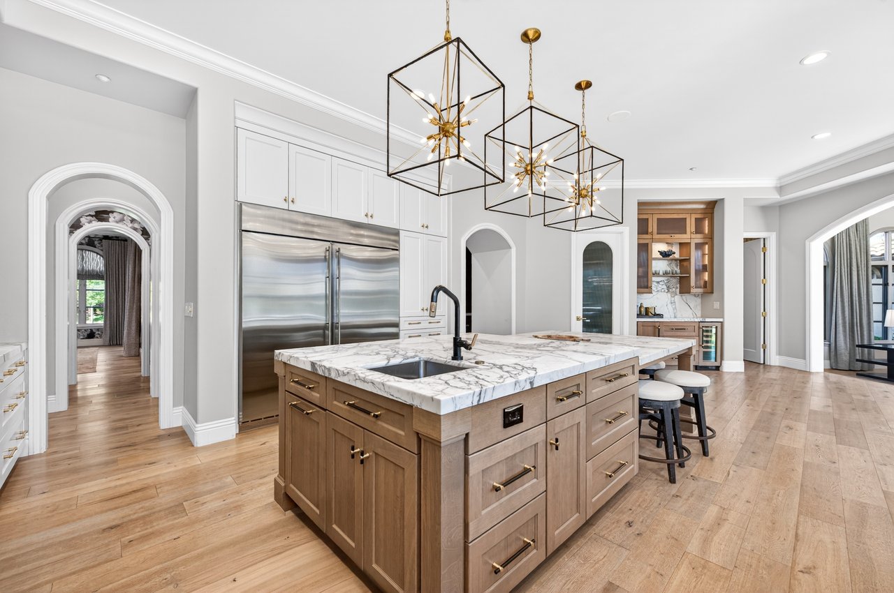 Kitchen with a large marble-topped wood island, stainless steel refrigerator, and geometric pendant lights.