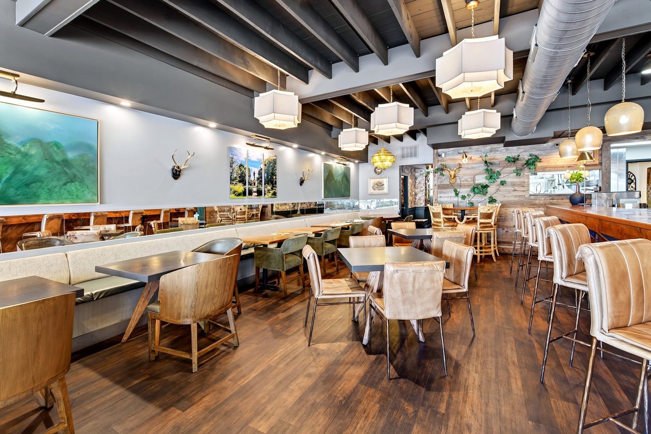 Restaurant dining room with booth seating, wooden tables, exposed beams, and pendant lights.