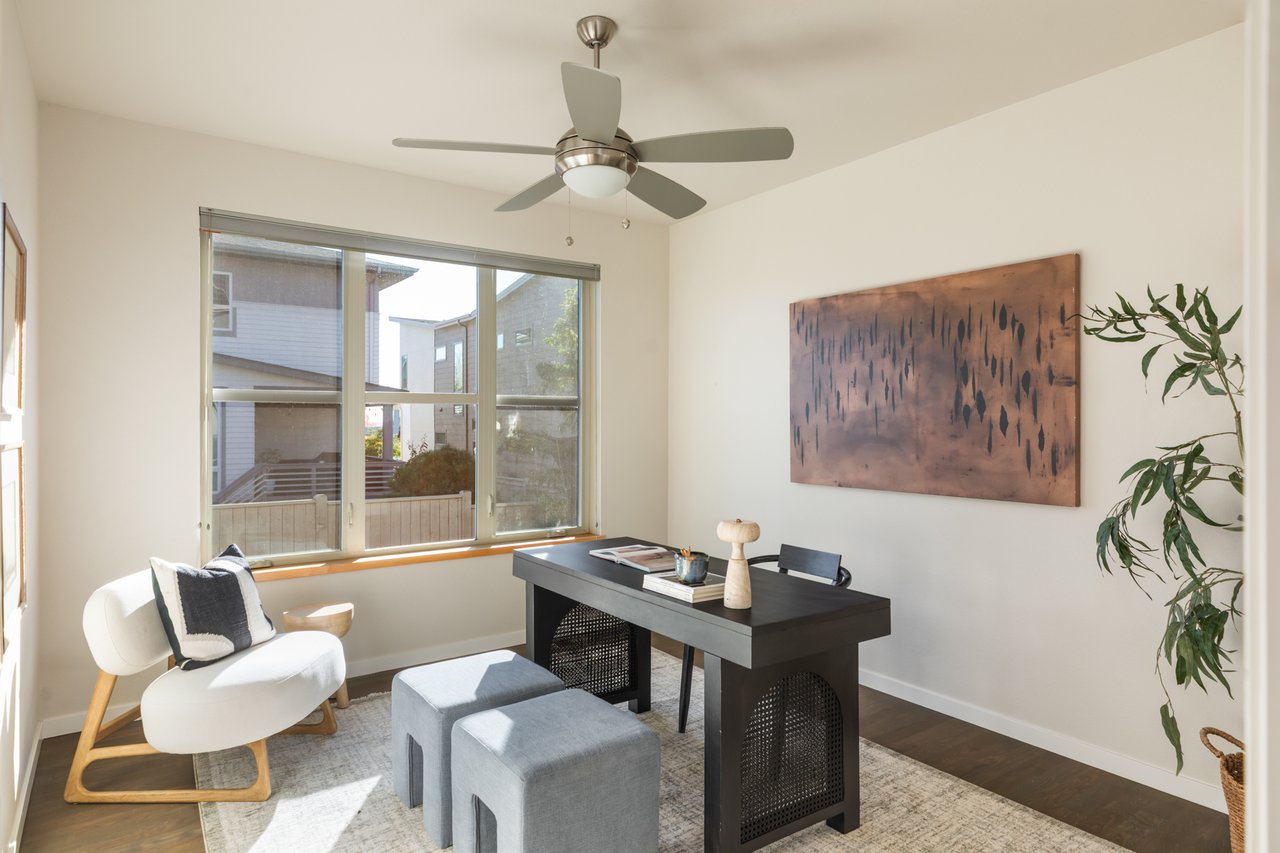 Home office with a desk, ceiling fan, white accent chair, and large window