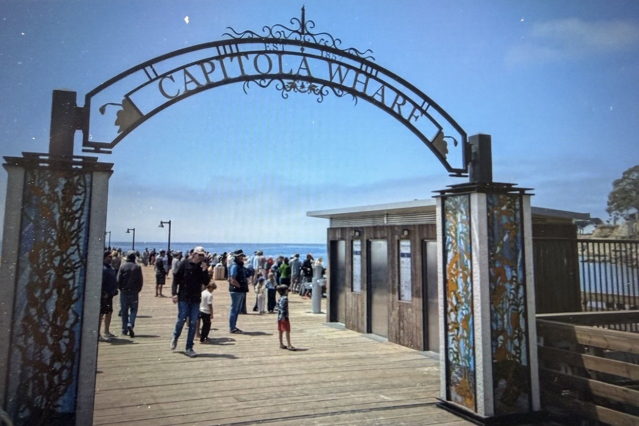 Capitola Wharf entrance arch framing visitors on the wooden pier and ocean beyond.