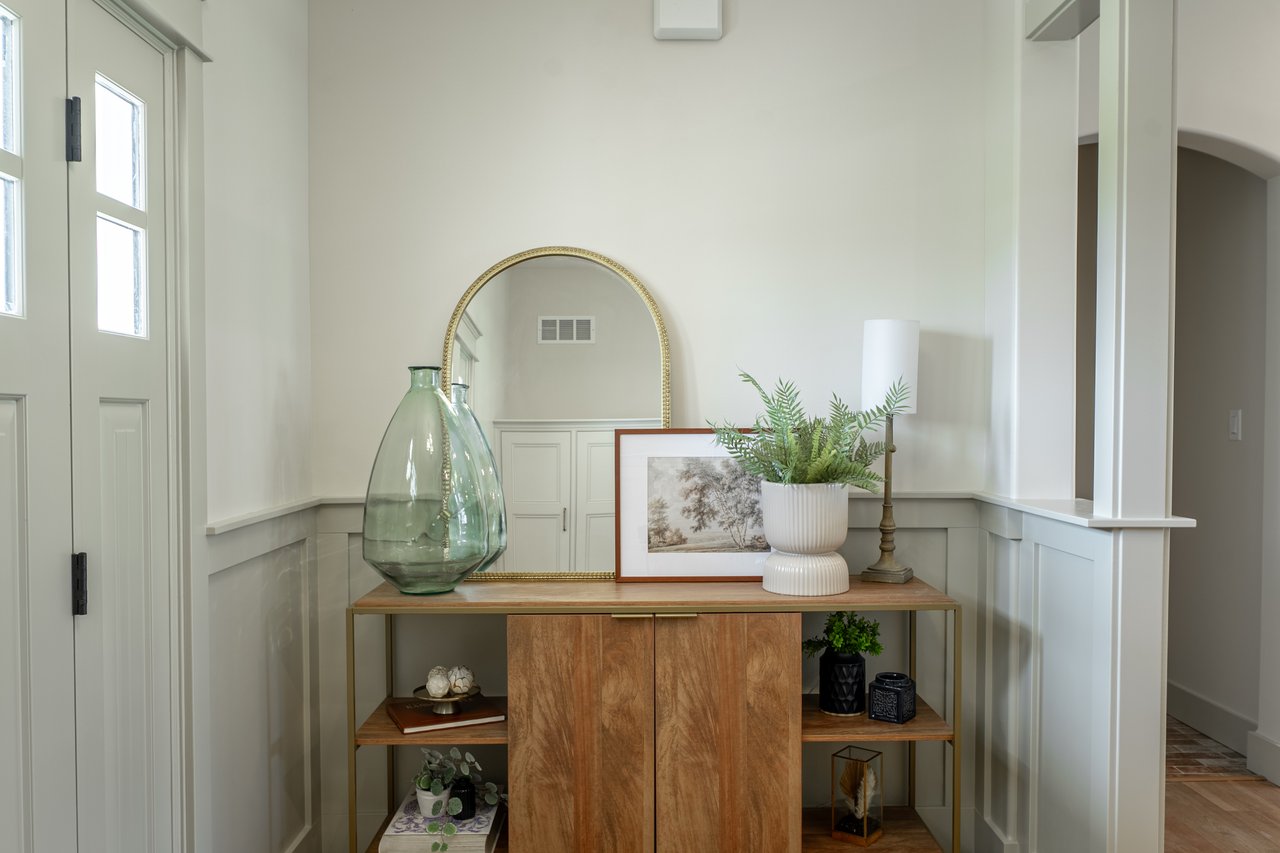 Entry foyer with a wood console, arched mirror, green glass vases, and potted fern.