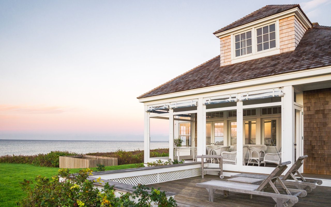 Coastal house with a glass porch and deck overlooking the ocean at sunset.