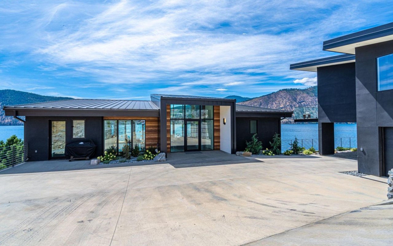 A modern, dark-colored house with large glass windows and wooden accents, featuring a flat roof