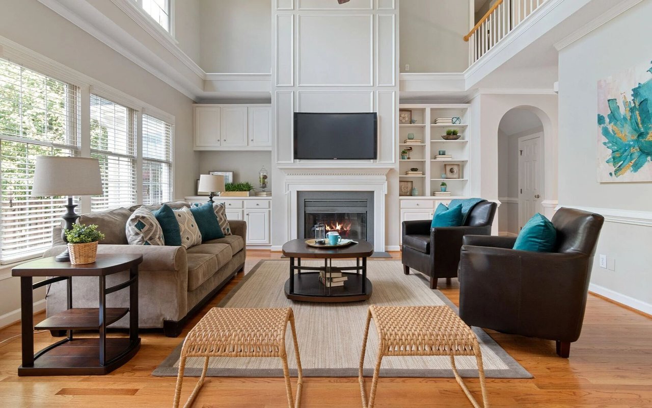 Living room with a fireplace, built-in shelving, tall windows, and teal-accented seating.