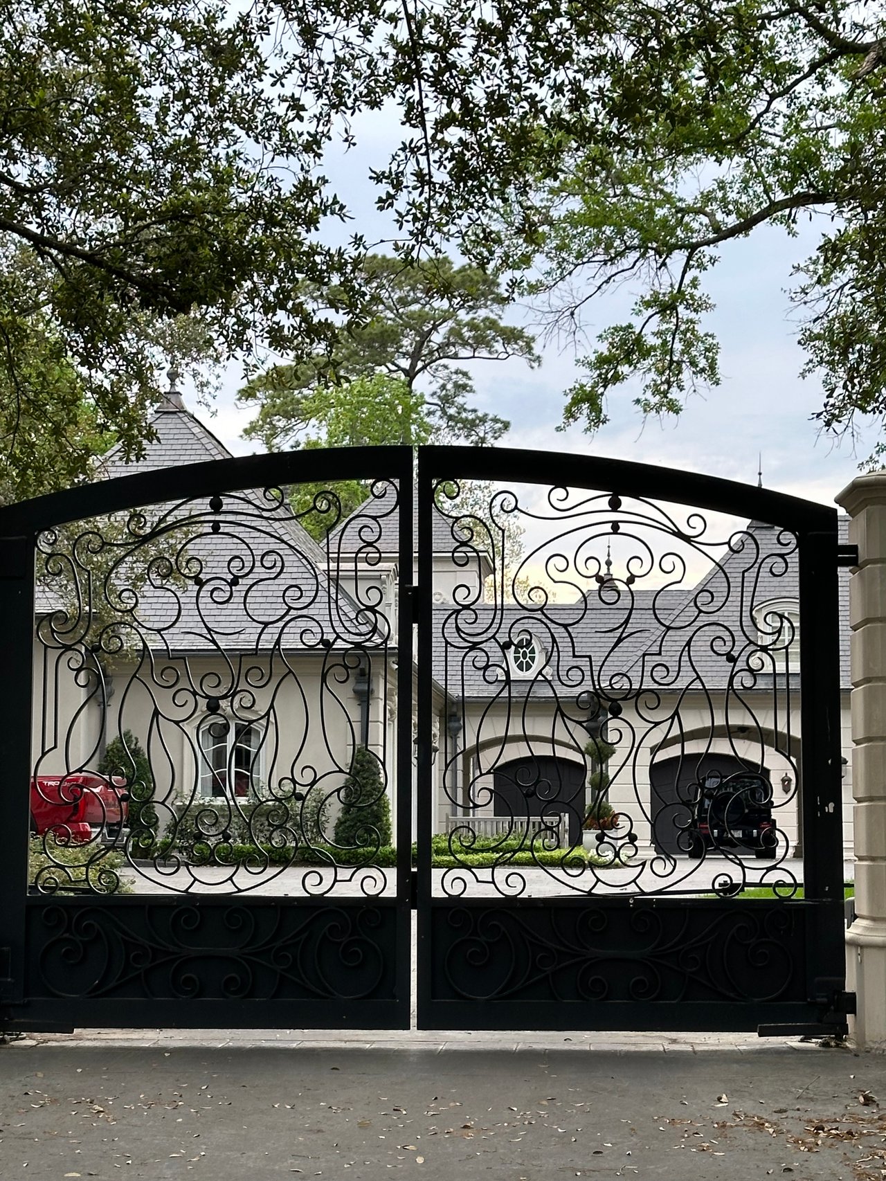 Metal double scroll gated Luxury home with slate roof and large oak trees