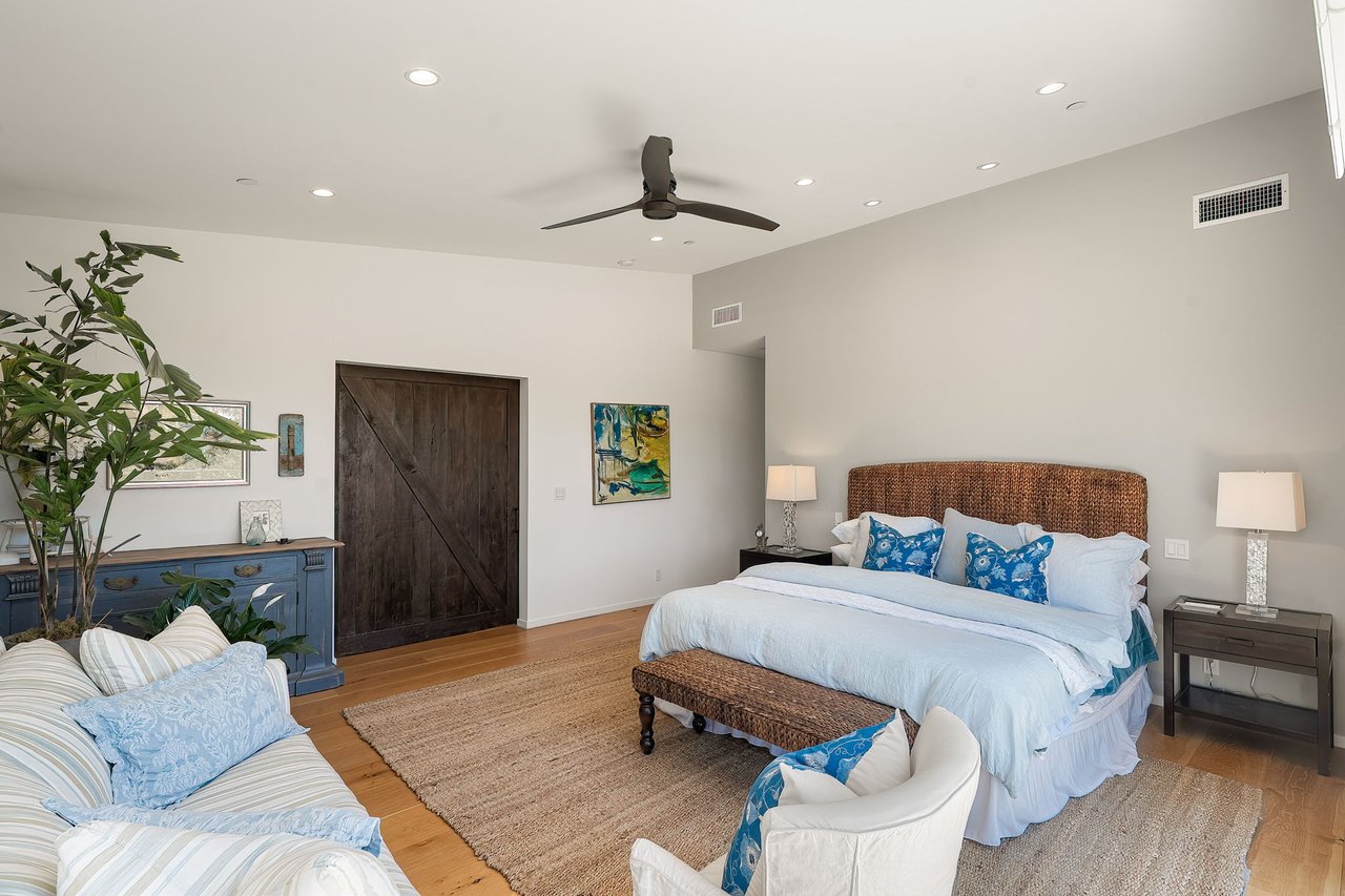 Furnished bedroom with a woven-headboard bed, blue-and-white linens, and a dark wood barn door.