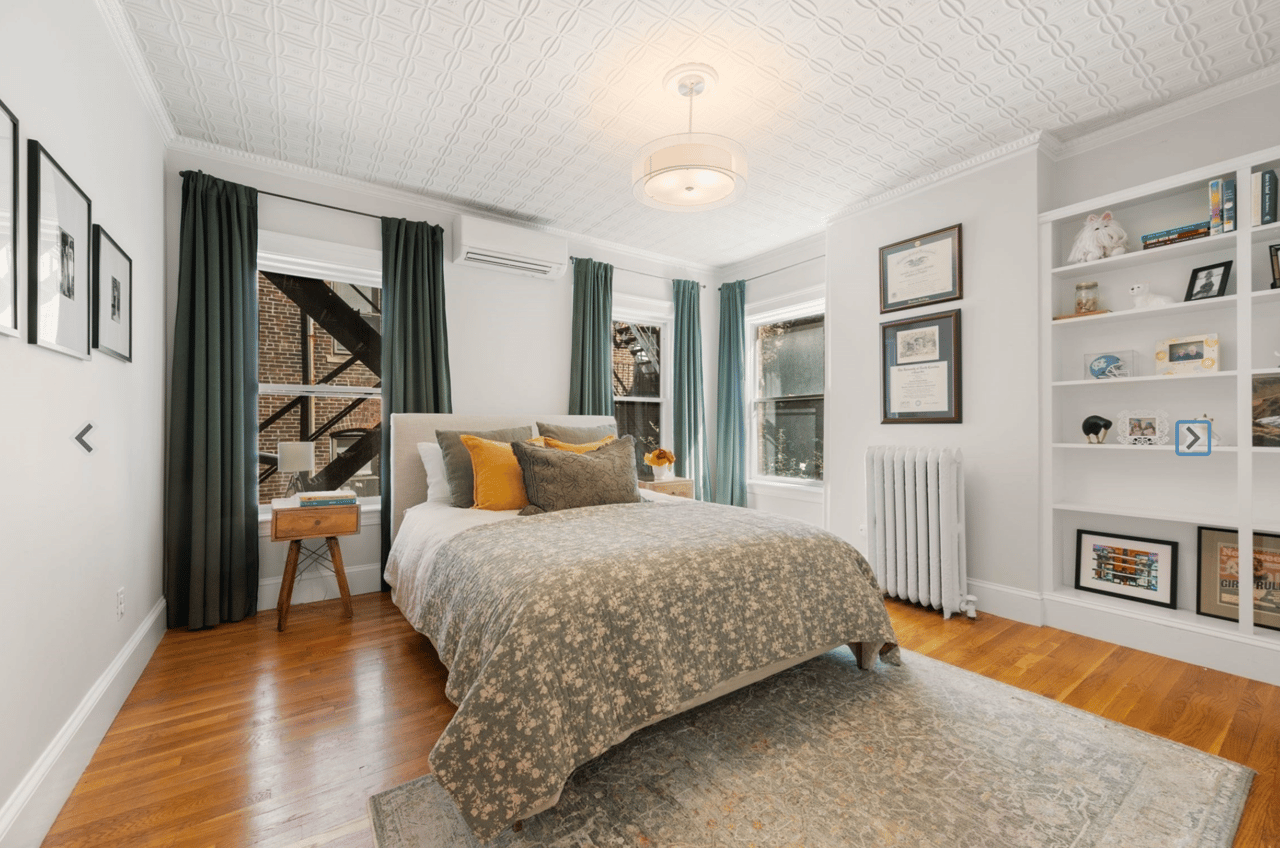 Bedroom with a large bed, patterned ceiling, hardwood floors, and built-in shelves.