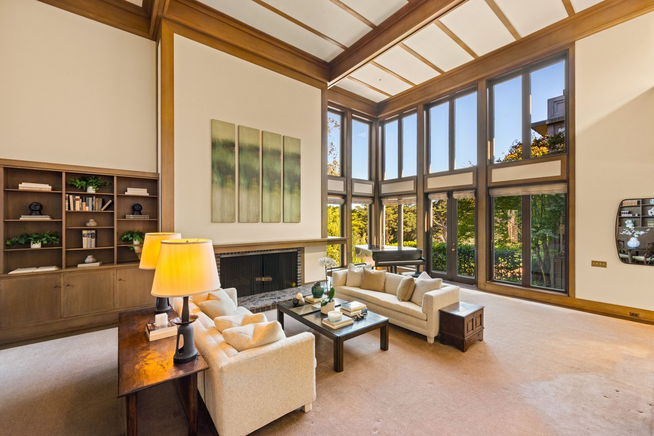 Living room with a beamed ceiling, tall windows, fireplace, and cream sofas.