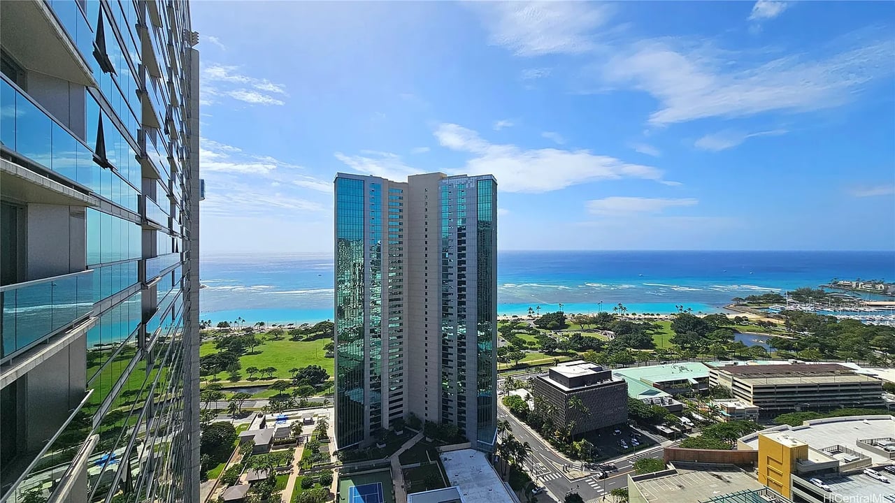 High-rise ocean view with neighboring towers, green parkland, and a bright blue sky.