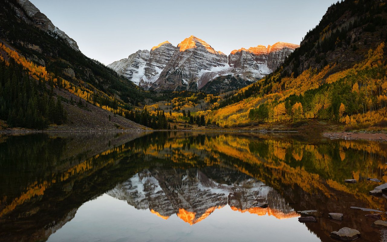 The Maroon Bells glow above a lake reflecting autumn aspens near Aspen.
