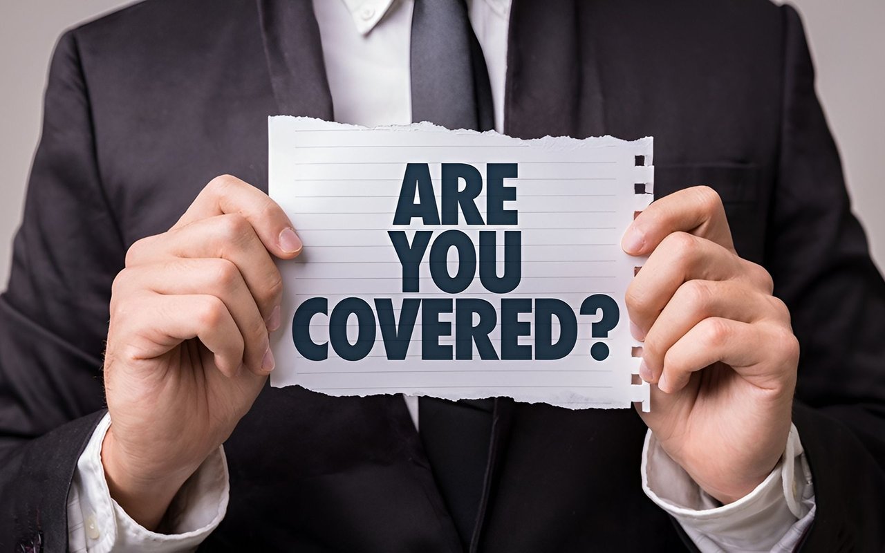 A person in a dark suit holds a sign asking, “Are you covered?”