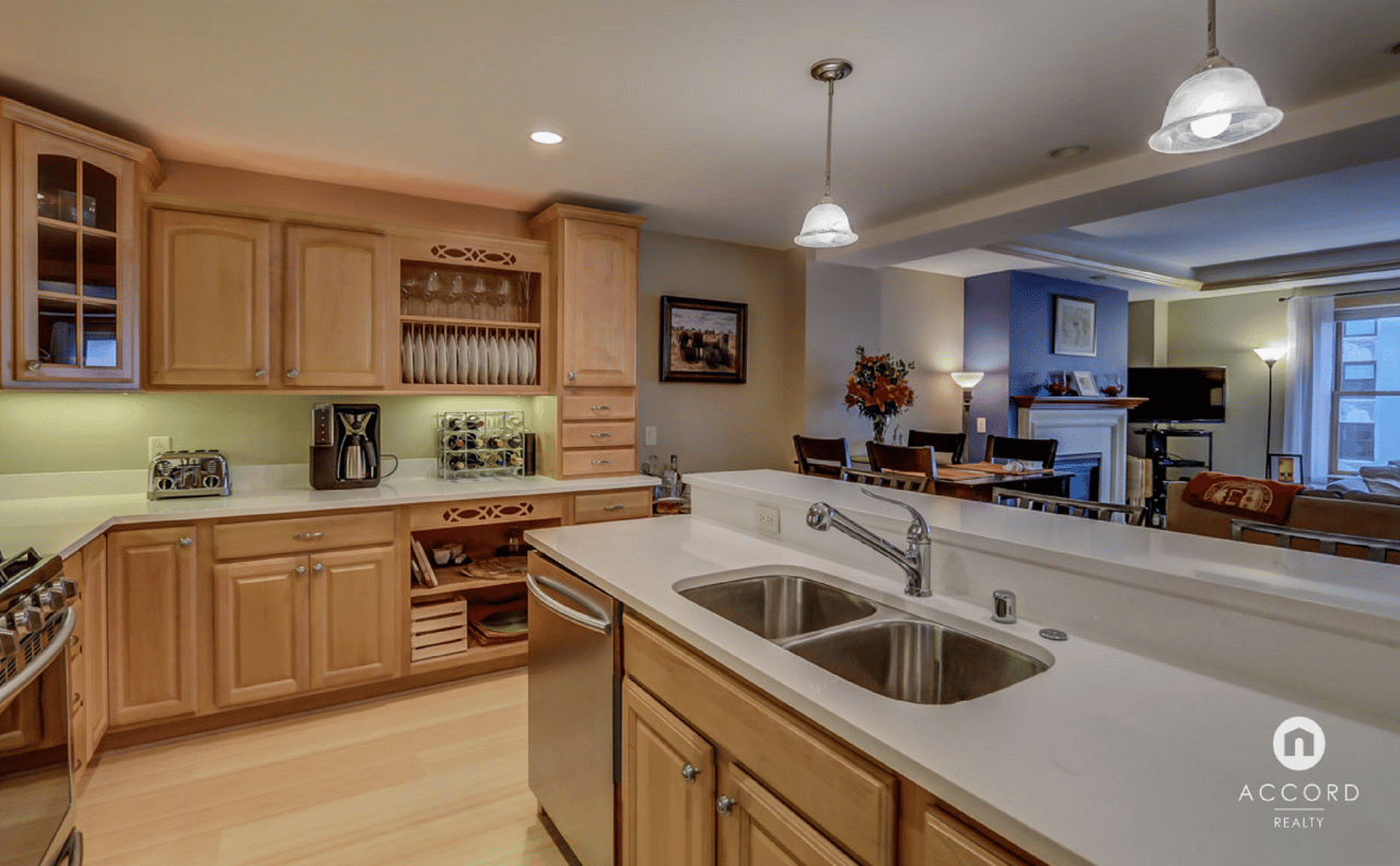 Condo kitchen with honey-colored cabinets, a white counter, and an open view into the dining and living areas.