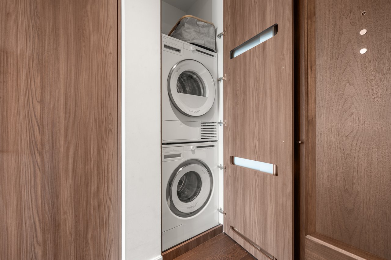 Stacked washer and dryer in a laundry closet with open wood-grain cabinet doors.
