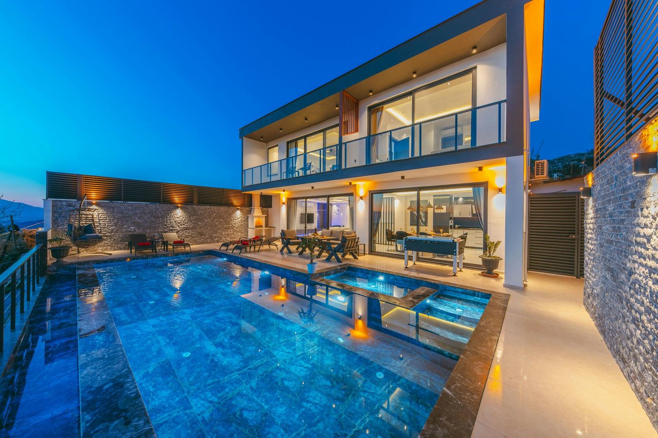 Luxury modern villa with illuminated swimming pool, outdoor lounge area, and contemporary architecture at night