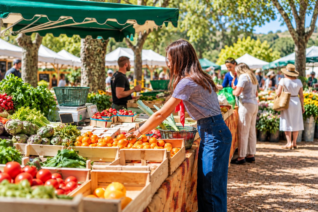 Woman selecting leafy greens among colorful produce at an outdoor farmers market.