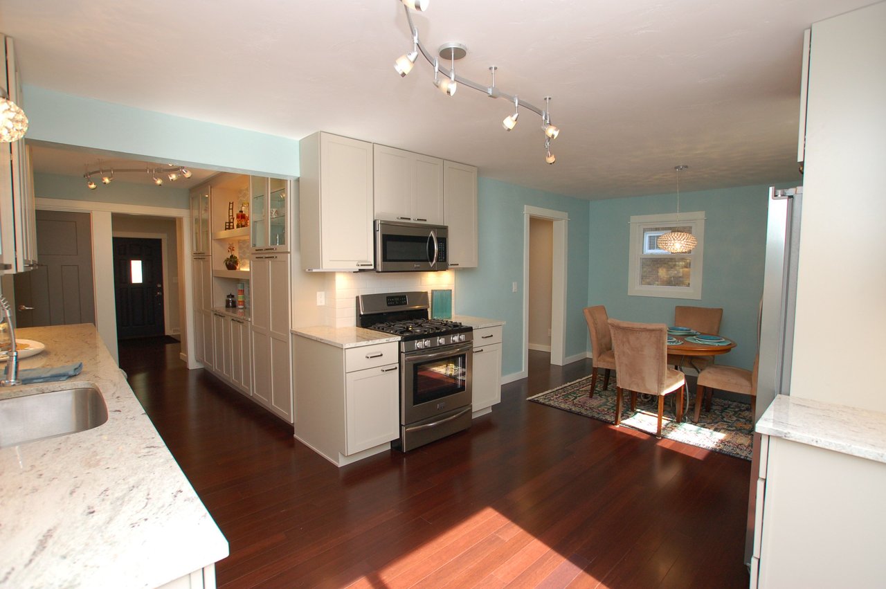 Open kitchen and dining area with white cabinets, stainless steel appliances, and a sunlit table.