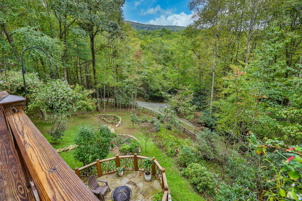 View from a wooden deck over a landscaped garden and stone fire pit patio in Holly Forest, Sapphire, NC