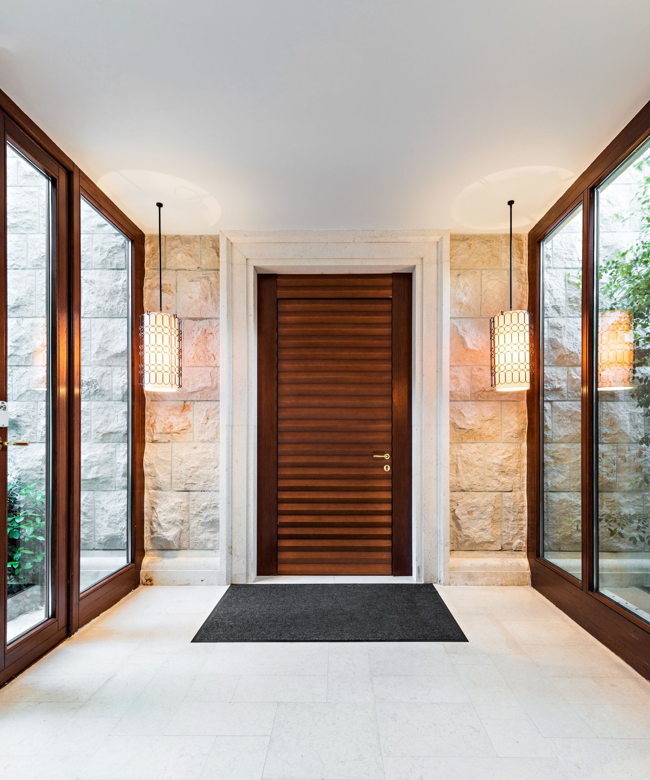 Stone-framed entryway with a dark wood door, tall windows, and matching pendant lights.