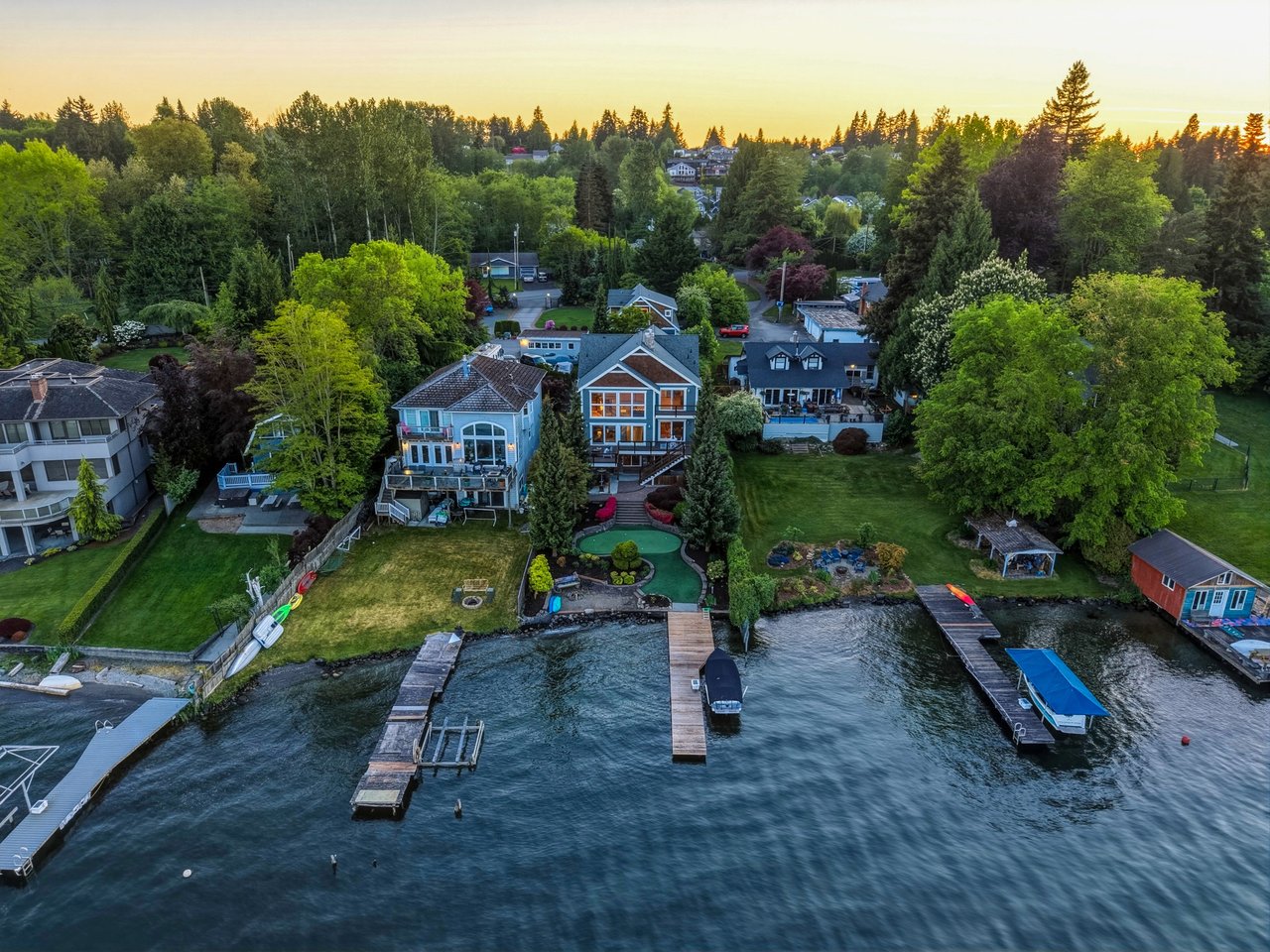Aerial view of waterfront homes with private docks and boats along a wooded shoreline.