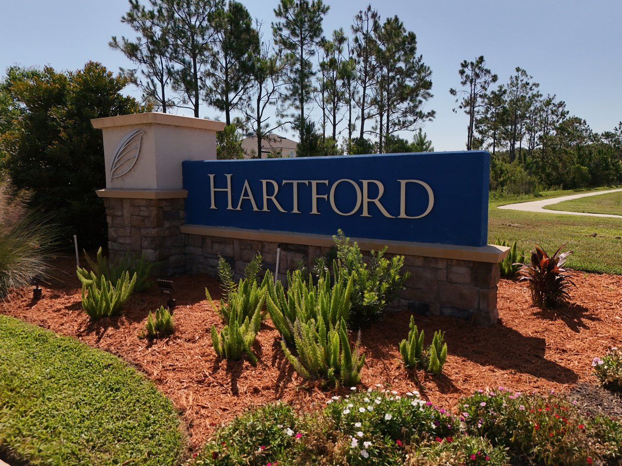 Hartford neighborhood entrance sign beside landscaped grounds and pine trees.