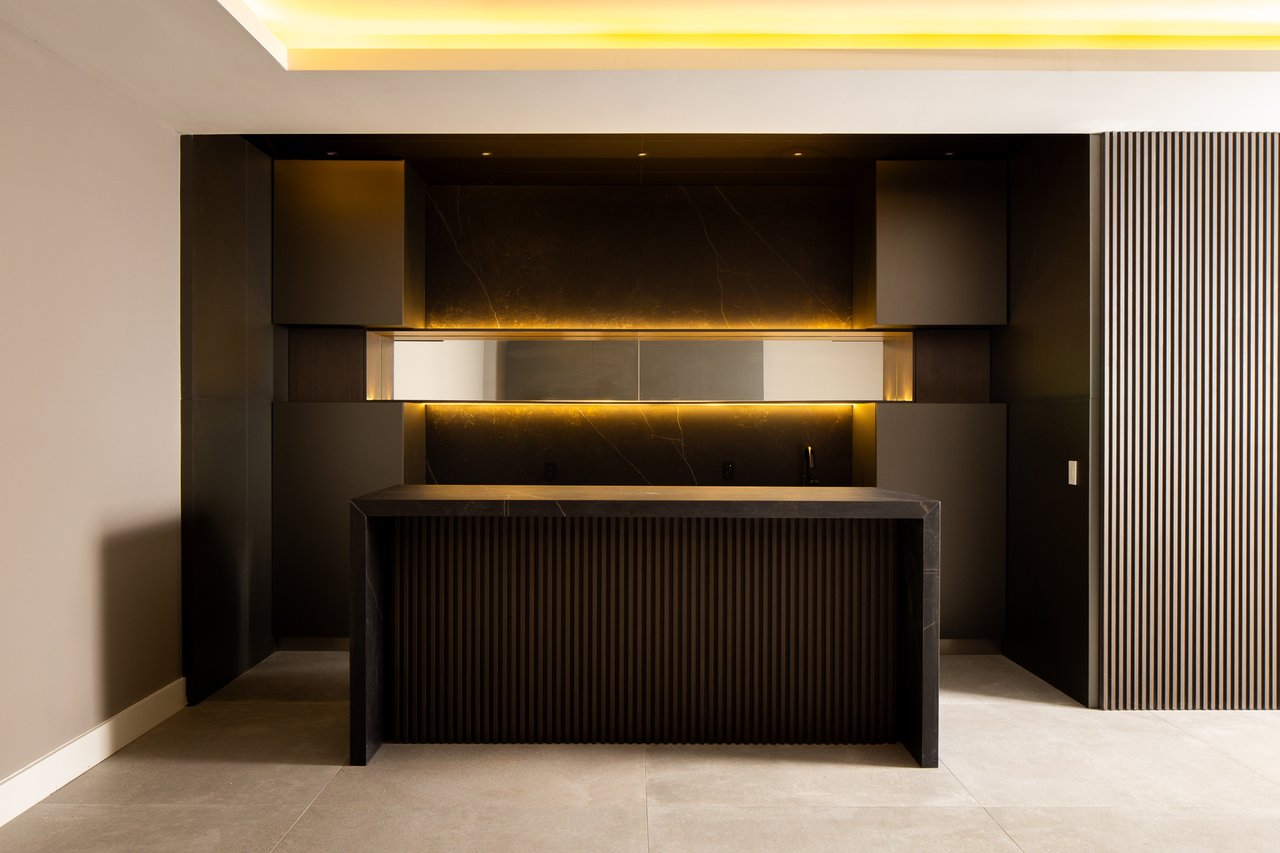 Modern dark kitchen with a fluted stone island and warm backlit backsplash.